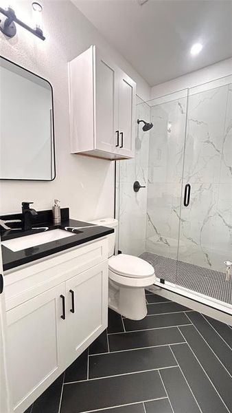 Bathroom featuring a shower with door, vanity, tile patterned flooring, and toilet