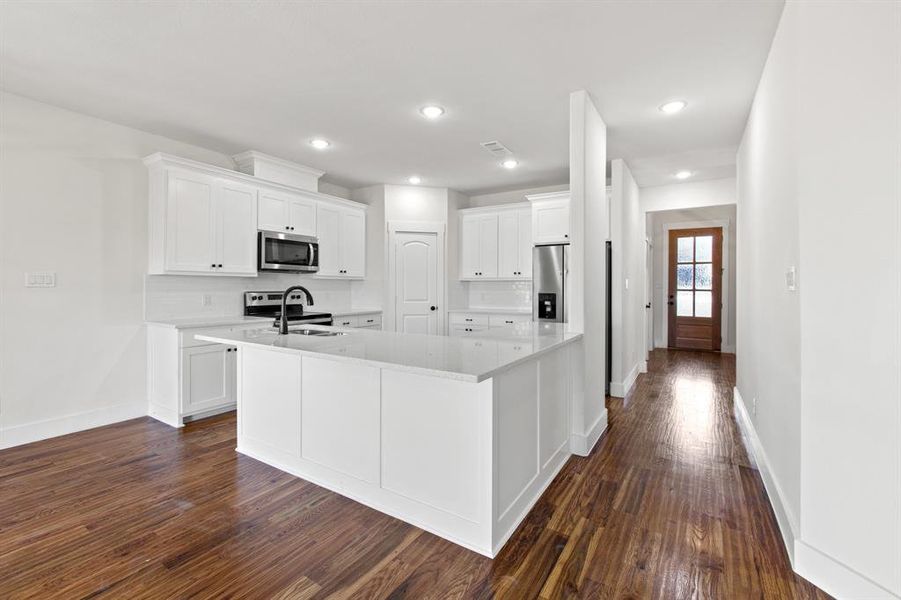 Kitchen featuring white cabinets, appliances with stainless steel finishes, dark hardwood / wood-style floors, and an island with sink