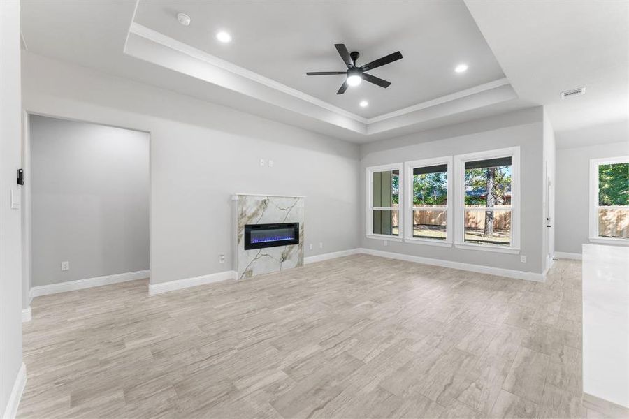 Unfurnished living room with ceiling fan, a raised ceiling, and a healthy amount of sunlight