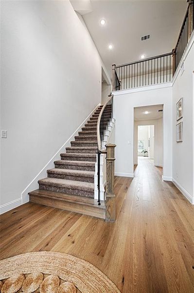 Stairway with light hardwood / wood-style floors and a towering ceiling