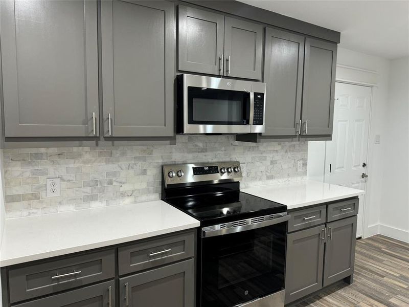 Kitchen with appliances with stainless steel finishes, dark hardwood / wood-style flooring, backsplash, and gray cabinetry