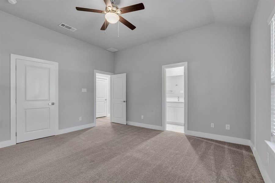 Unfurnished bedroom with vaulted ceiling, light carpet, ceiling fan, and ensuite bathroom