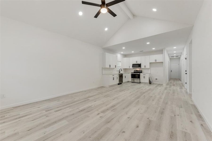 Unfurnished living room with high vaulted ceiling, sink, ceiling fan, beam ceiling, and light hardwood / wood-style floors