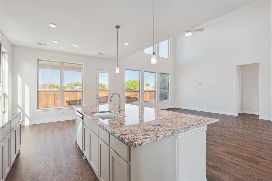 Kitchen with decorative light fixtures, an island with sink, dark wood-type flooring, stainless steel dishwasher, and sink