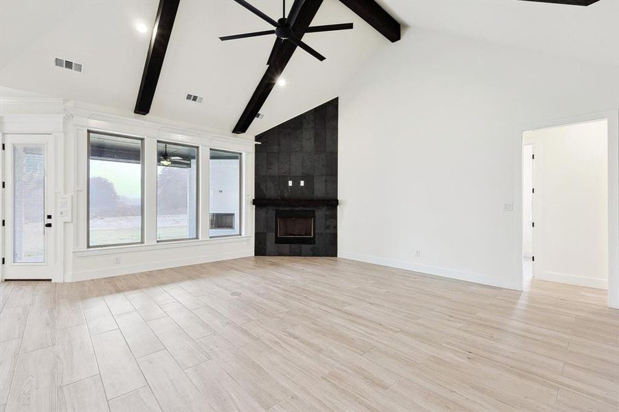 Unfurnished living room with high vaulted ceiling, a fireplace, light wood-type flooring, beam ceiling, and ceiling fan