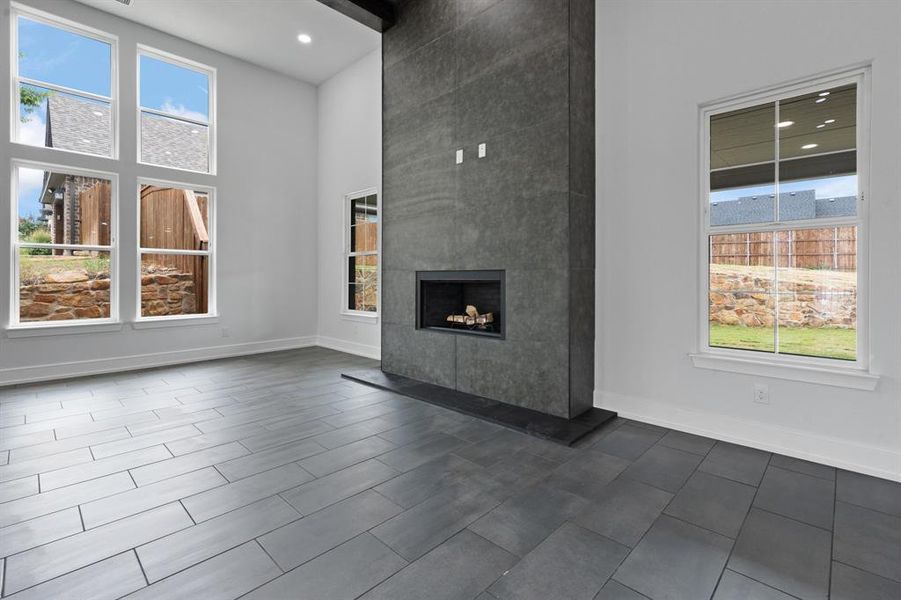 Unfurnished living room with plenty of natural light, dark tile patterned flooring, a large fireplace, and a towering ceiling