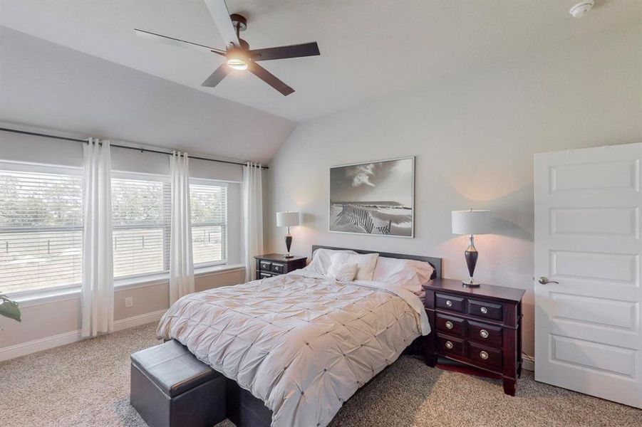 Carpeted bedroom featuring ceiling fan and vaulted ceiling