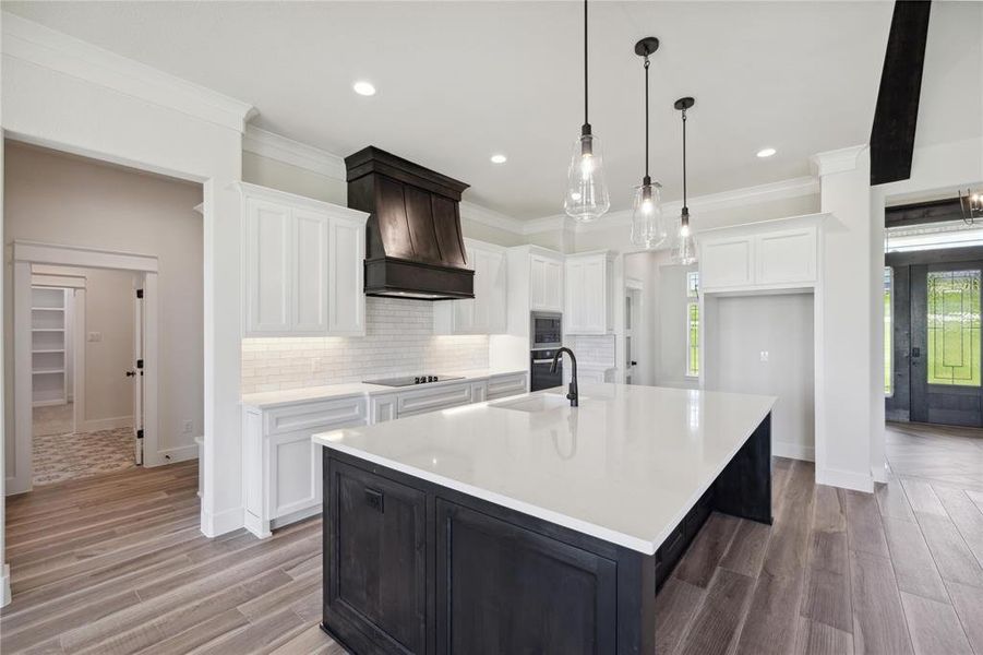 Kitchen featuring white cabinetry, a center island with sink, and custom range hood