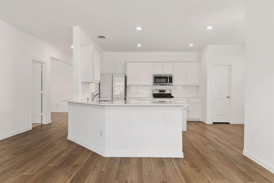 Kitchen with light hardwood / wood-style floors, kitchen peninsula, stove, tasteful backsplash, and white cabinetry