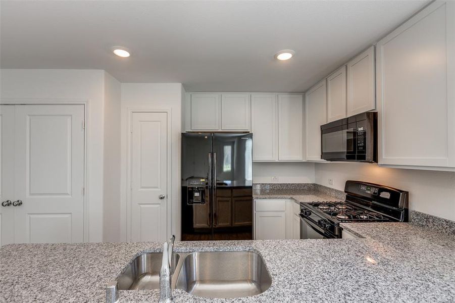 Kitchen featuring light stone countertops, sink, white cabinetry, and black appliances