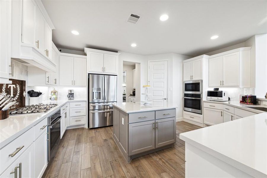 Kitchen features include a large island with accent color, quartz counter tops, ceramic tile floor and undercabinet lighting.