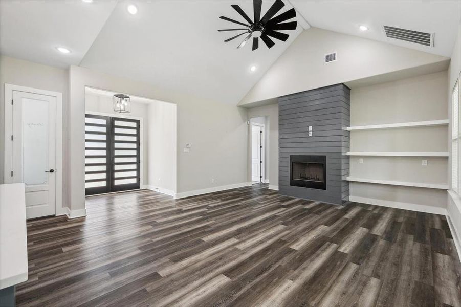 Unfurnished living room featuring dark hardwood / wood-style flooring, built in shelves, high vaulted ceiling, ceiling fan, and a large fireplace