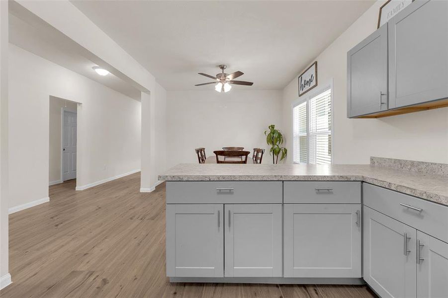 The photo shows a spacious kitchen. It features a ceiling fan, recessed lighting, dining area, and a large window that allows great natural light to beam through.