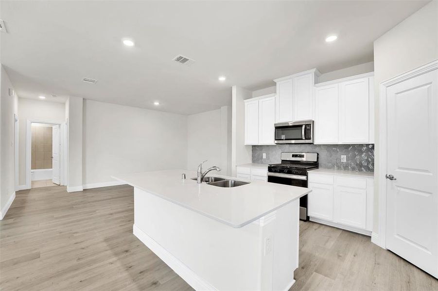 Kitchen featuring light hardwood / wood-style flooring, a center island with sink, white cabinetry, appliances with stainless steel finishes, and sink