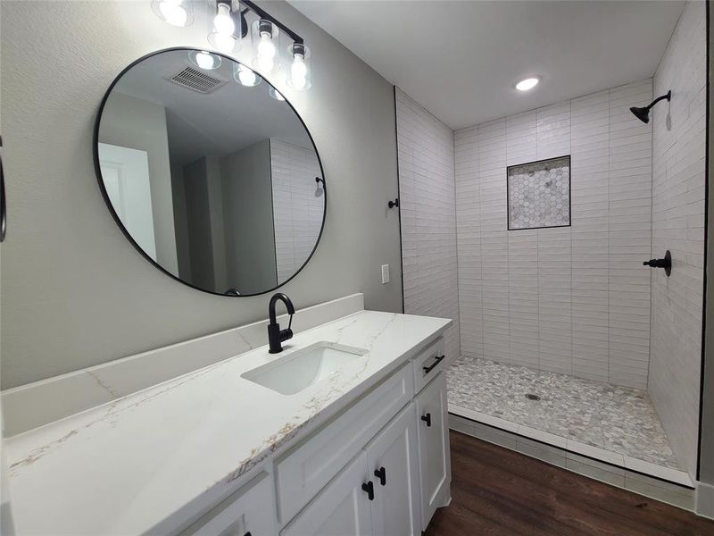 Primary Bathroom with wood-type flooring, a tile shower, and vanity