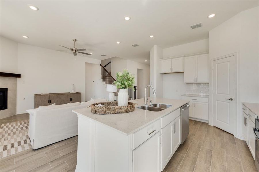 Kitchen with sink, an island with sink, white cabinetry, a fireplace, and ceiling fan