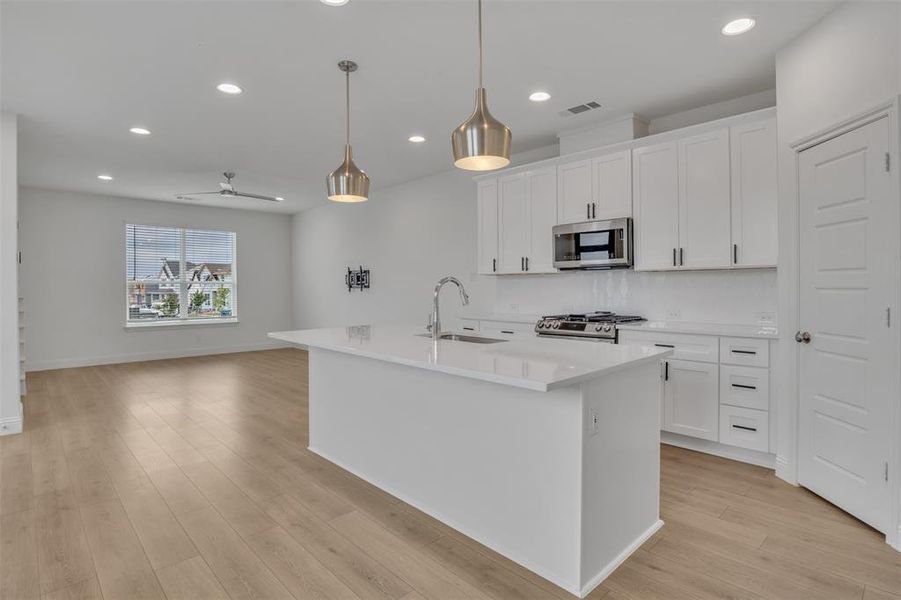 Kitchen with light hardwood / wood-style flooring, an island with sink, white cabinets, sink, and appliances with stainless steel finishes