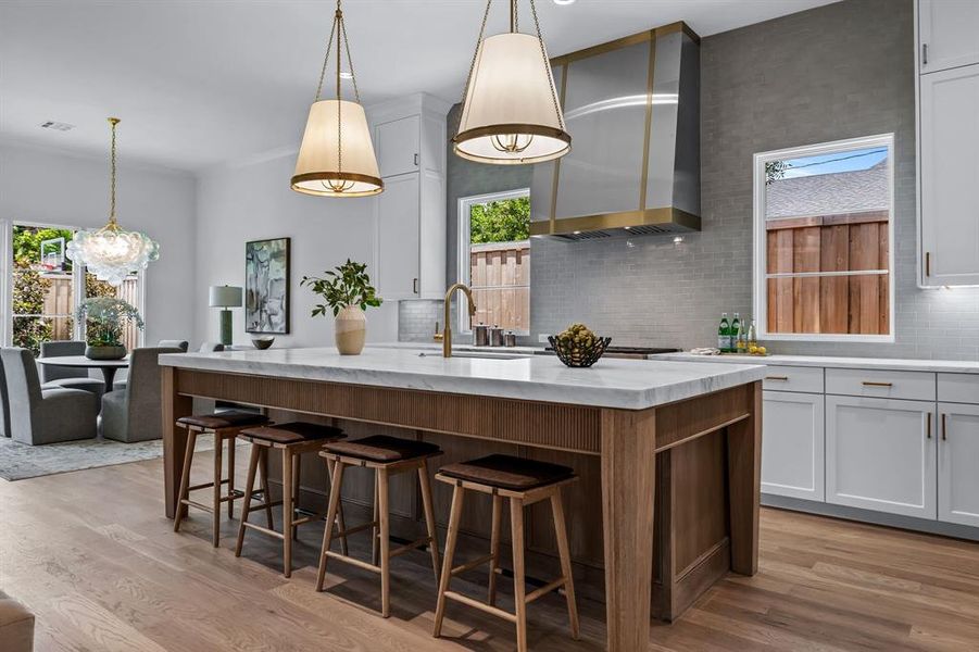 Kitchen with an island with sink, light wood-type flooring, backsplash, wall chimney range hood, and sink