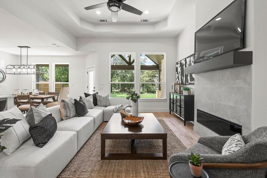 Living room featuring light wood-type flooring, a tray ceiling, ceiling fan, and a tile fireplace