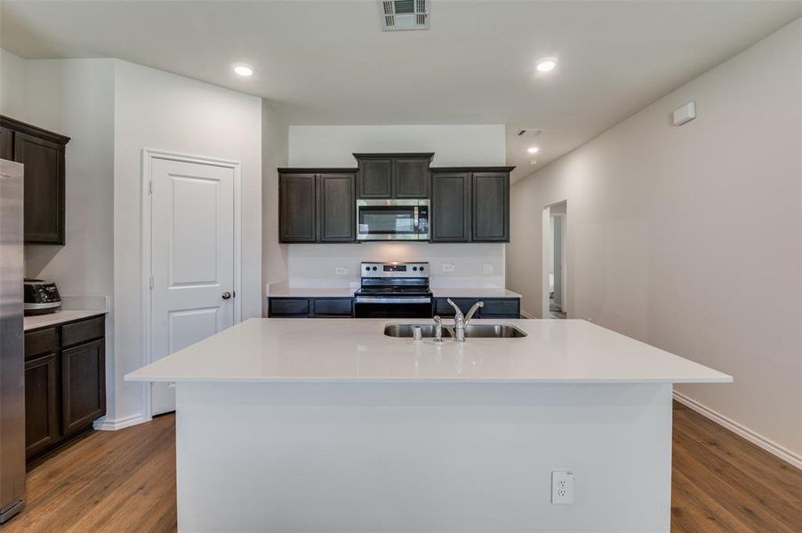 Kitchen with appliances with stainless steel finishes, hardwood / wood-style floors, sink, and a center island with sink