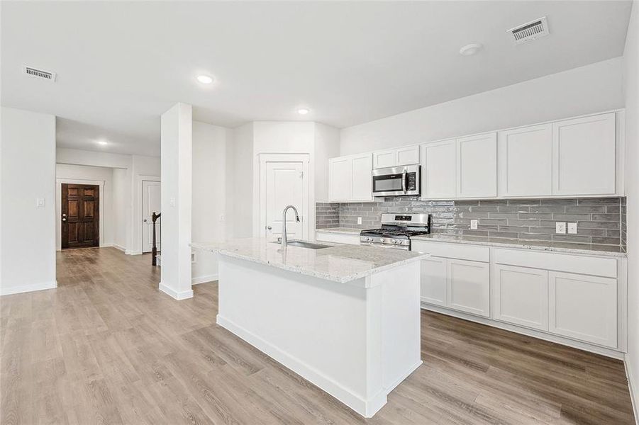 Kitchen featuring appliances with stainless steel finishes, light hardwood / wood-style flooring, tasteful backsplash, sink, and white cabinetry