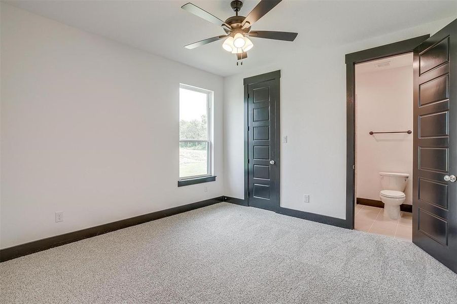 Unfurnished bedroom featuring light colored carpet, ensuite bath, ceiling fan, and a closet