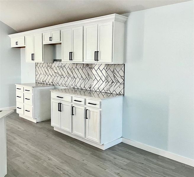 Kitchen featuring white cabinetry, decorative backsplash, and light wood-type flooring