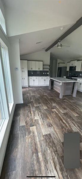 Unfurnished living room with ceiling fan, dark hardwood / wood-style floors, and vaulted ceiling with beams