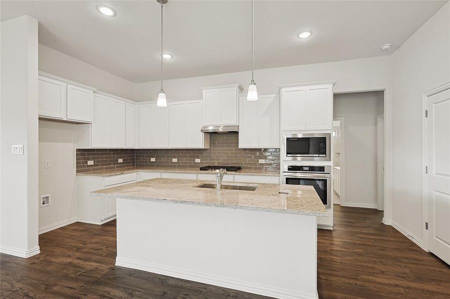 Kitchen with dark hardwood / wood-style flooring, appliances with stainless steel finishes, white cabinetry, and an island with sink