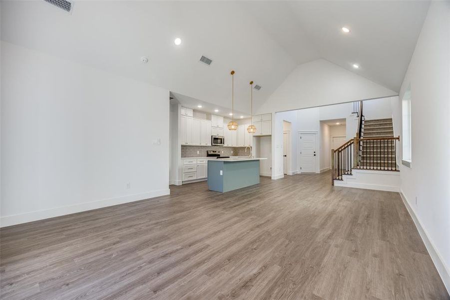 Unfurnished living room featuring light wood-type flooring, high vaulted ceiling, and sink