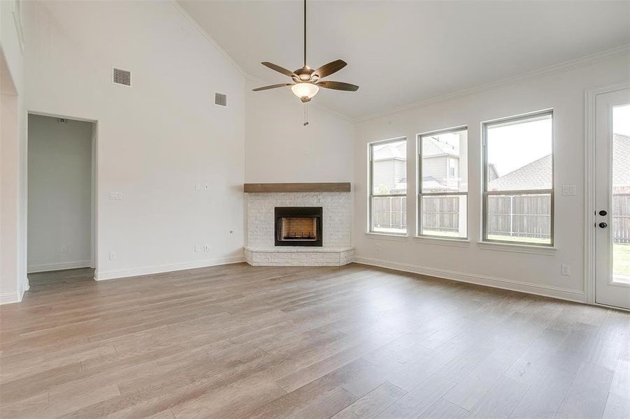 Unfurnished living room with light hardwood / wood-style floors, ornamental molding, a brick fireplace, and high vaulted ceiling