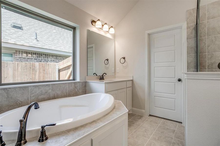 Bathroom with vanity, tile patterned flooring, lofted ceiling, and tiled bath