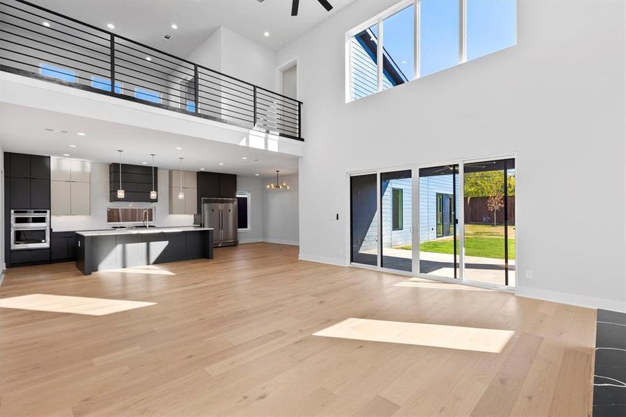 Unfurnished living room with sink, a towering ceiling, light hardwood / wood-style floors, and ceiling fan with notable chandelier