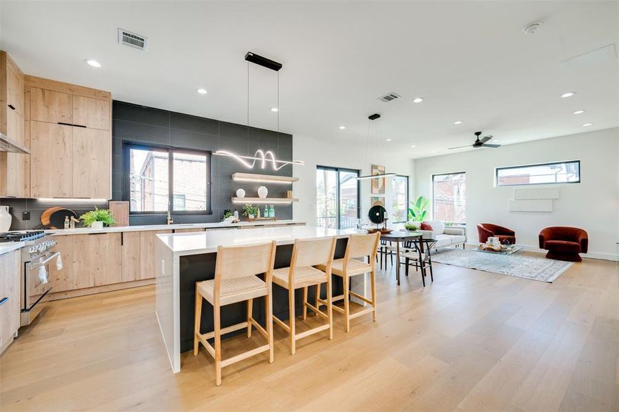 Kitchen featuring high end stainless steel range oven, light brown cabinetry, light wood-type flooring, pendant lighting, and a center island