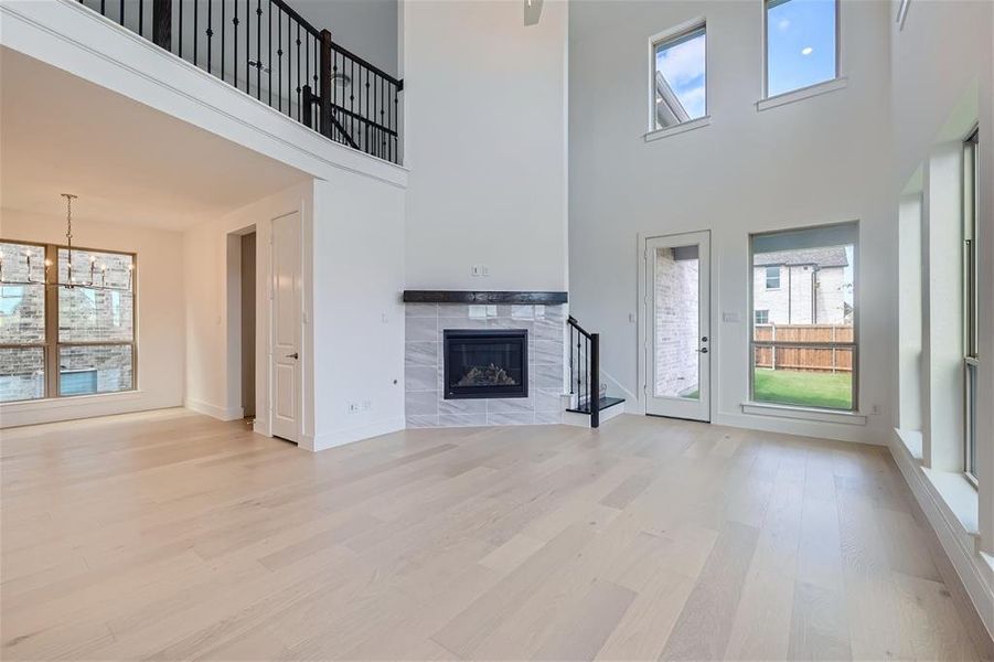 Living room featuring light wood-type flooring, a tiled fireplace, a towering ceiling, and an inviting chandelier