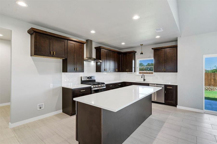 Kitchen featuring dark brown cabinets, sink, a kitchen island, wall chimney range hood, and appliances with stainless steel finishes