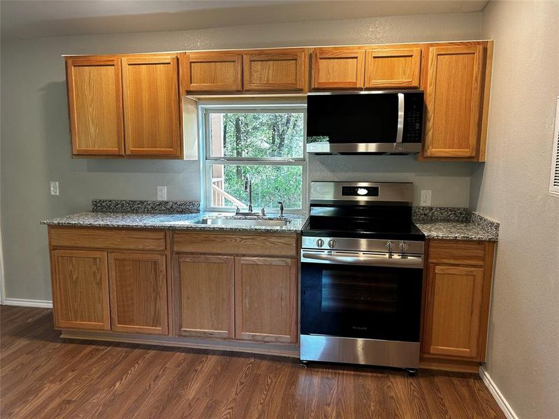 Kitchen featuring light stone counters, appliances with stainless steel finishes, dark hardwood / wood-style floors, and sink