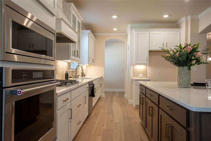 Kitchen featuring stainless steel appliances, crown molding, sink, white cabinetry, and light hardwood / wood-style floors