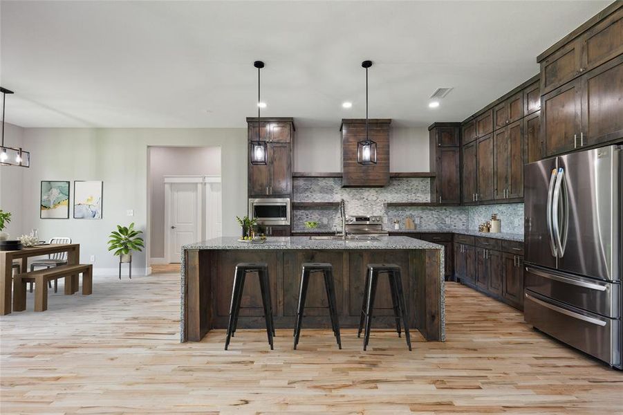 Kitchen with dark stone counters, dark brown cabinets, tasteful backsplash, stainless steel appliances, and light wood-type flooring