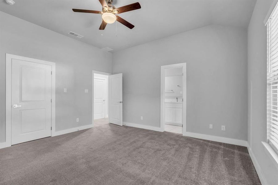 Unfurnished bedroom with carpet, vaulted ceiling, ensuite bath, and ceiling fan