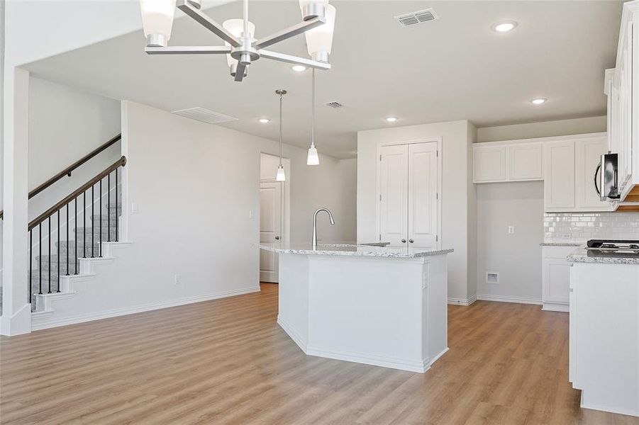 Kitchen featuring light wood-type flooring, white cabinetry, hanging light fixtures, decorative backsplash, and a center island with sink