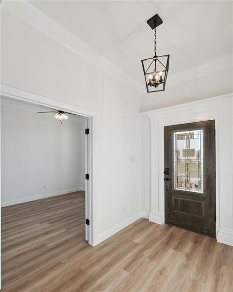 Foyer entrance featuring a notable chandelier, crown molding, and light wood-type flooring