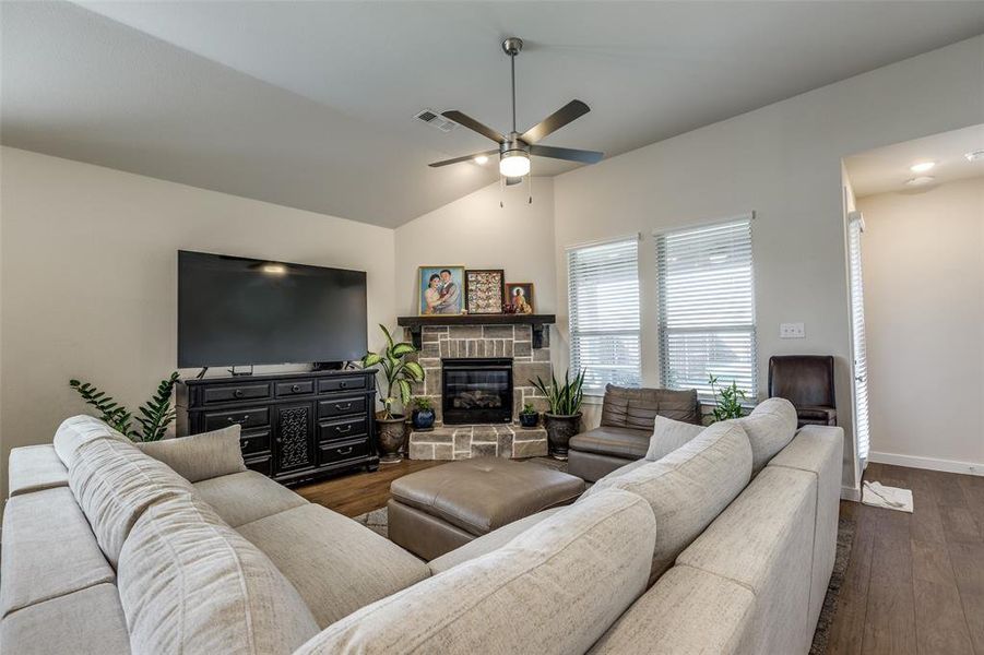 Living room with lofted ceiling, a stone fireplace, dark wood-type flooring, and ceiling fan