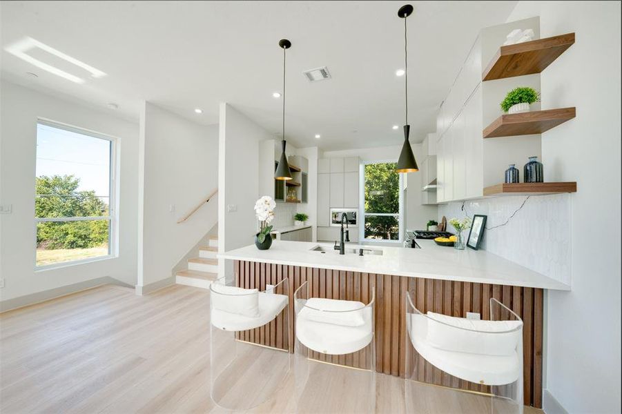 Kitchen featuring kitchen peninsula, hanging light fixtures, extractor fan, light wood-type flooring, and sink