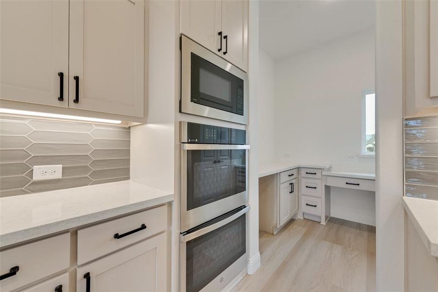 Kitchen featuring light hardwood / wood-style flooring, appliances with stainless steel finishes, tasteful backsplash, light stone counters, and white cabinets