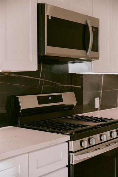 Kitchen featuring stainless steel appliances, white cabinets, and tasteful backsplash