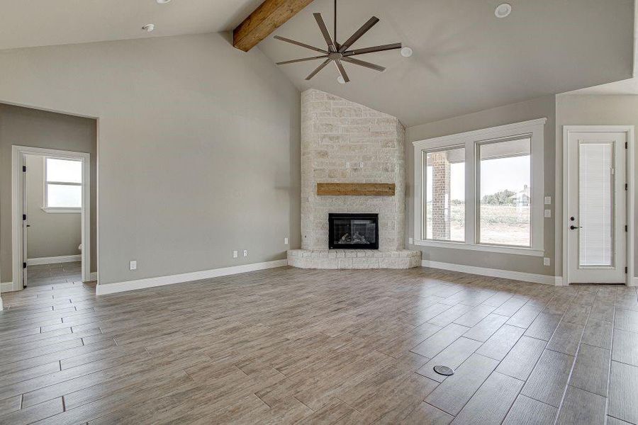 Unfurnished living room featuring brick wall, a stone fireplace, beam ceiling, ceiling fan, and light wood-type flooring