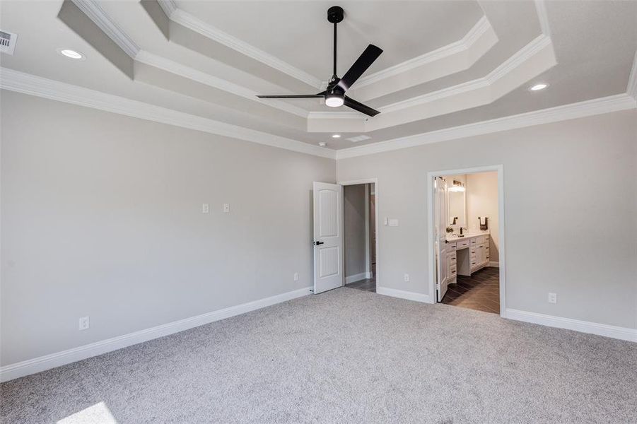 Master bedroom with ceiling fan, a double tray ceiling, connected bathroom, and crown molding