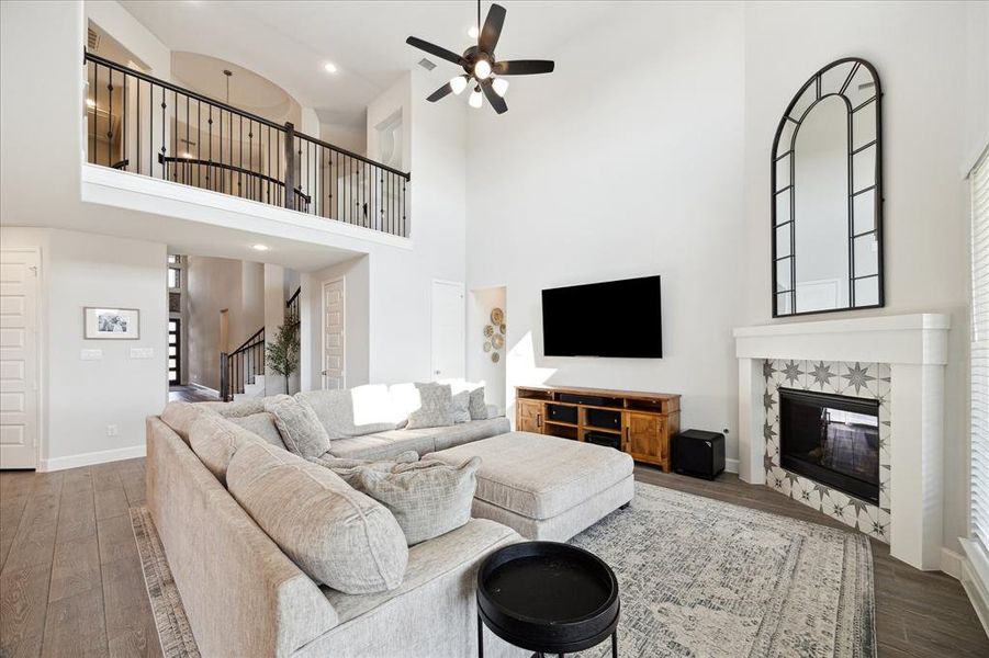 This is a spacious, high-ceilinged living room with an open second-story balcony,  a cozy fireplace, and contemporary decor.