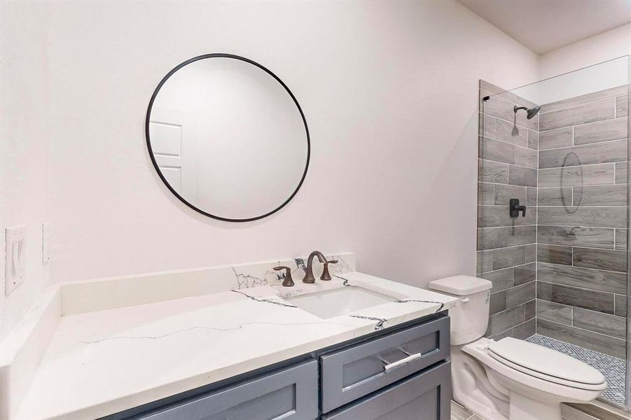 Bathroom featuring toilet, vanity, and a tile shower